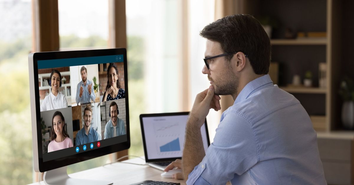 Ein Mann sitzt vor einem Computerbildschirm und hat eine Videokonferenz mit anderen Personen. Auf dem Bildschirm deren Gesichter.